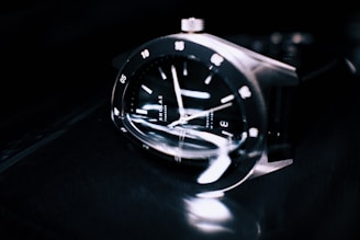 Close-up of a sleek luxury watch face with subtle reflections on a dark background.