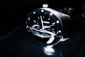 Close-up of a sleek black metallic watch reflecting soft white light.