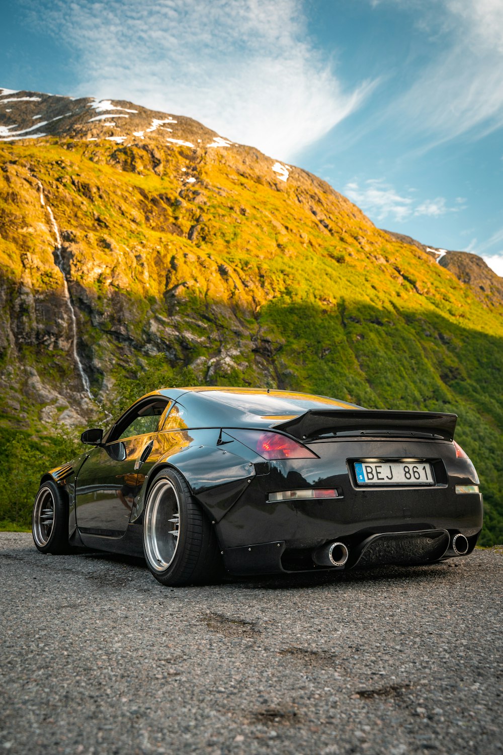 a black sports car parked on a gravel road with a mountain in the background