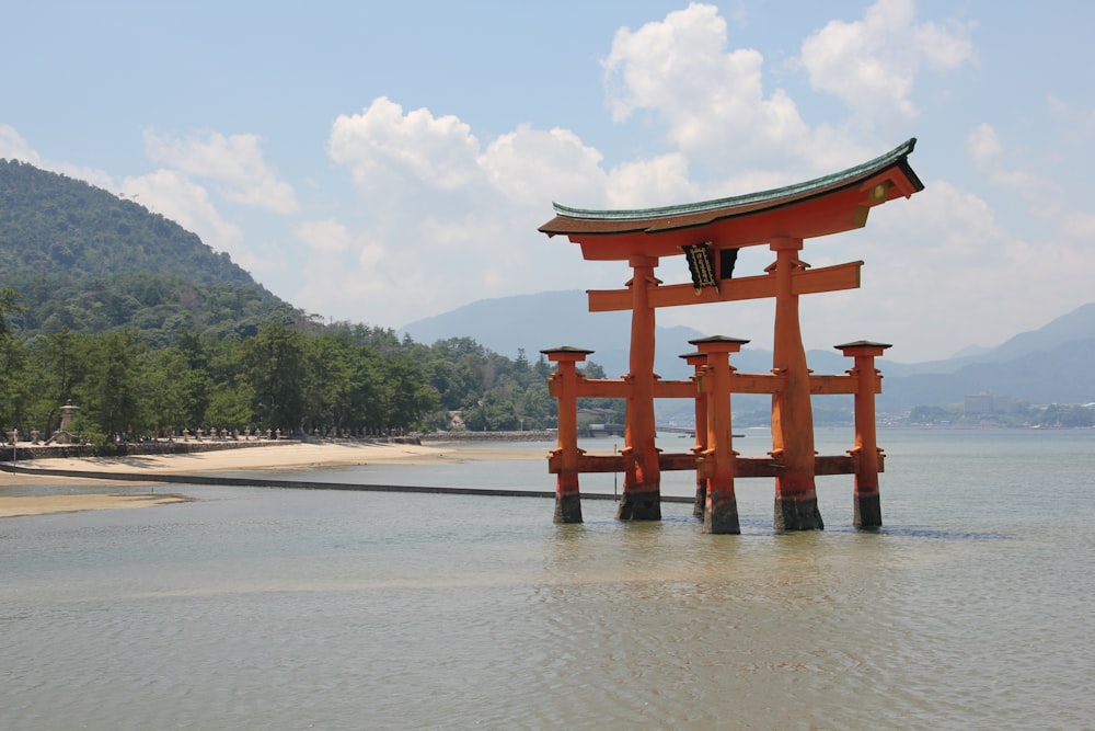 a red structure in the middle of a body of water with Itsukushima in the background