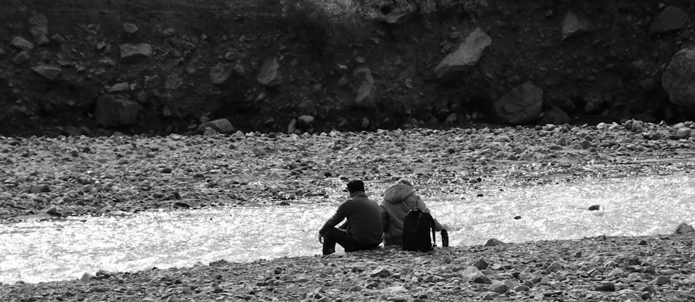 a man and a woman sitting on a rocky beach