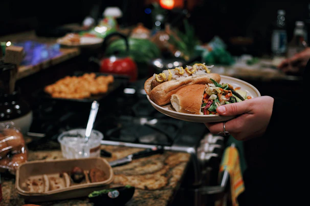 A close-up of a hand passing a tray with a hot dog, popcorn, and ice cream to a happy young softball player.