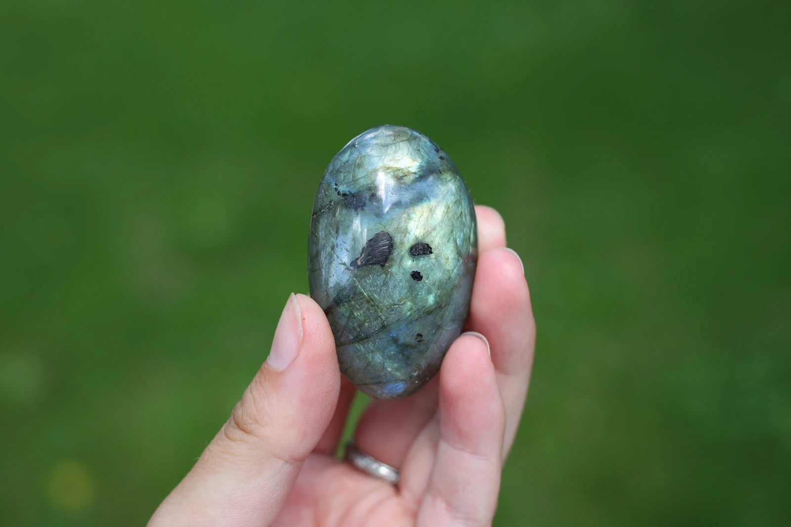 A hand holding a labradorite stone catching a blue flash of light
