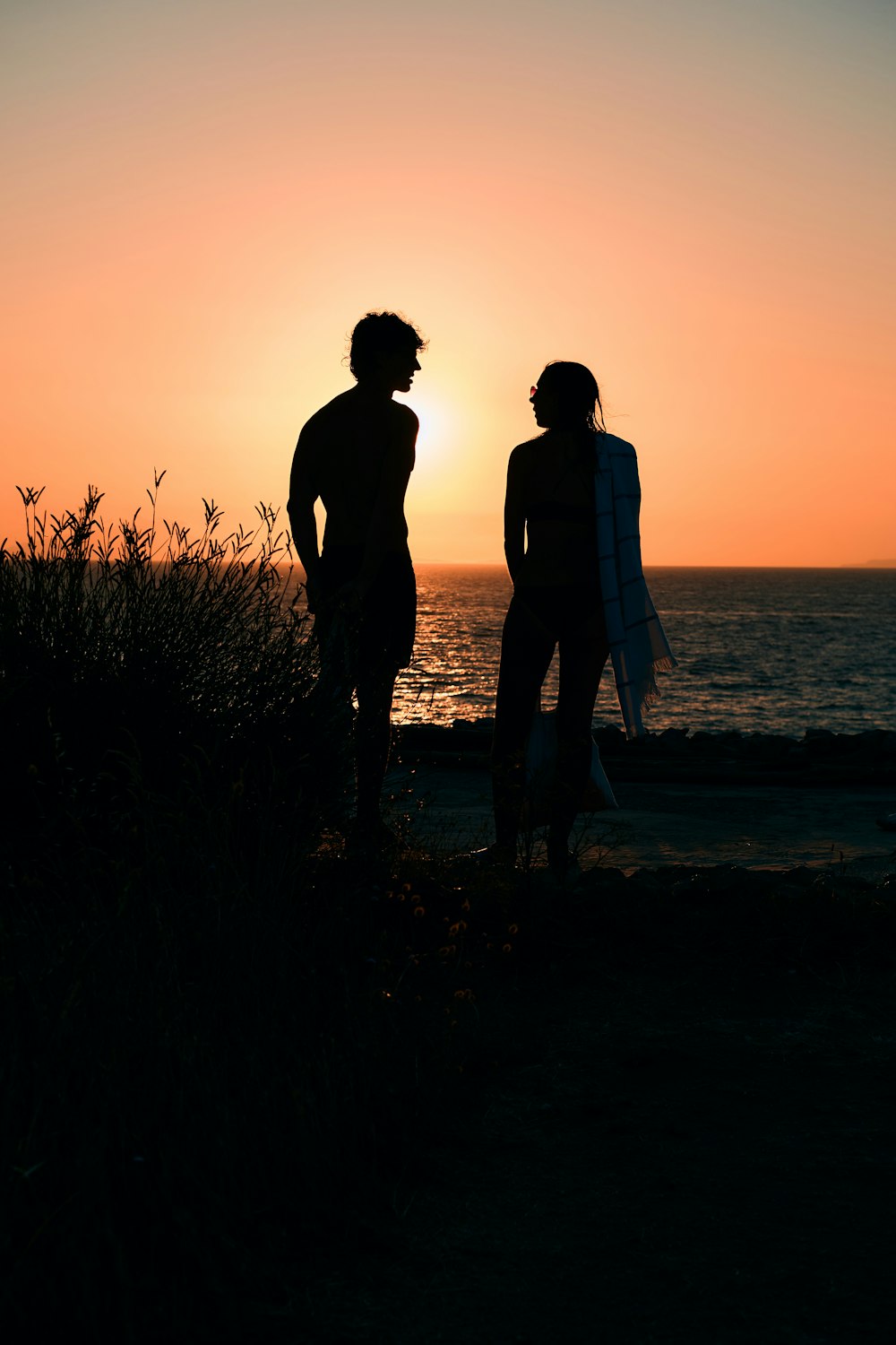 a man and woman walking on the beach at sunset