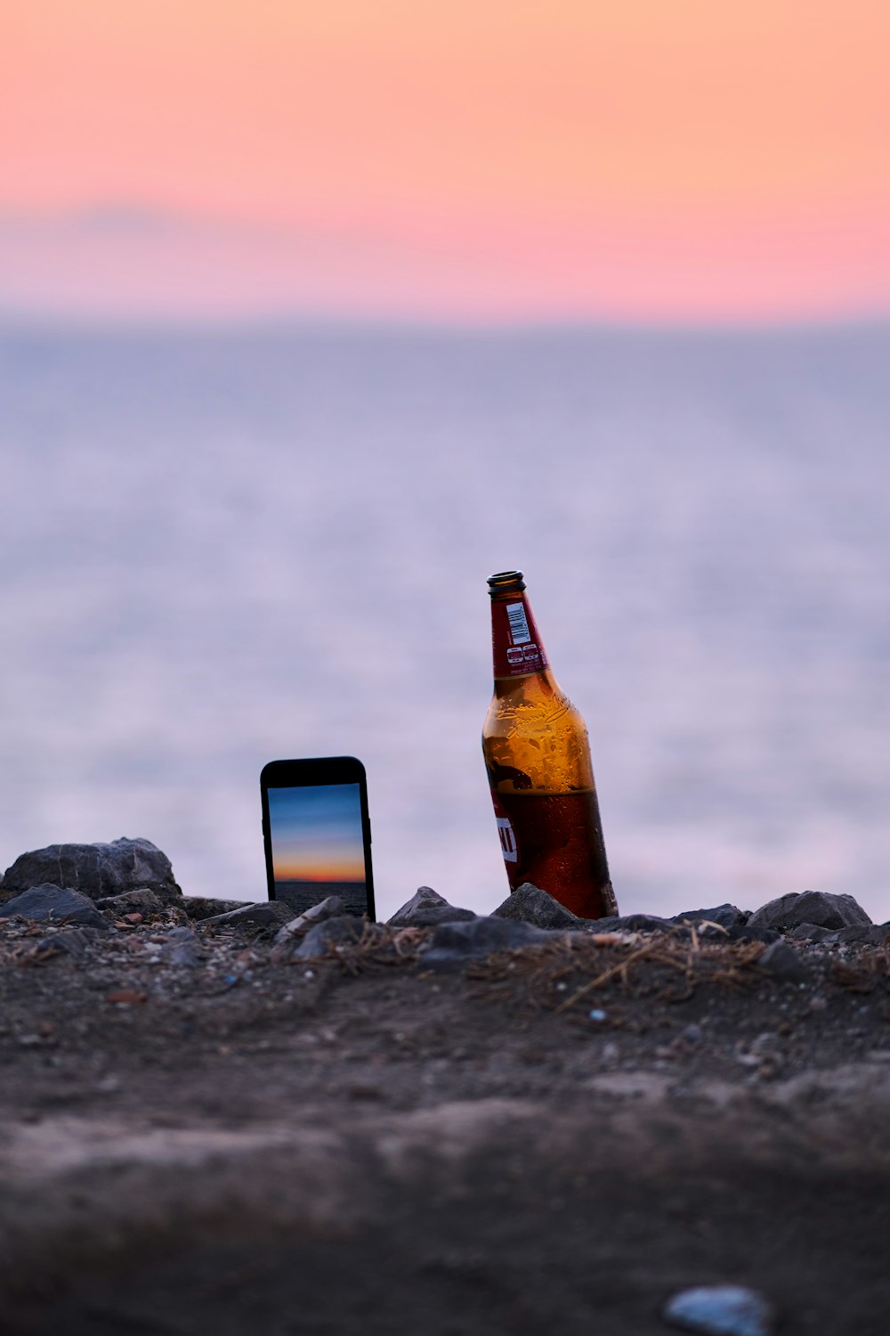 a bottle of beer and a laptop on a rocky surface