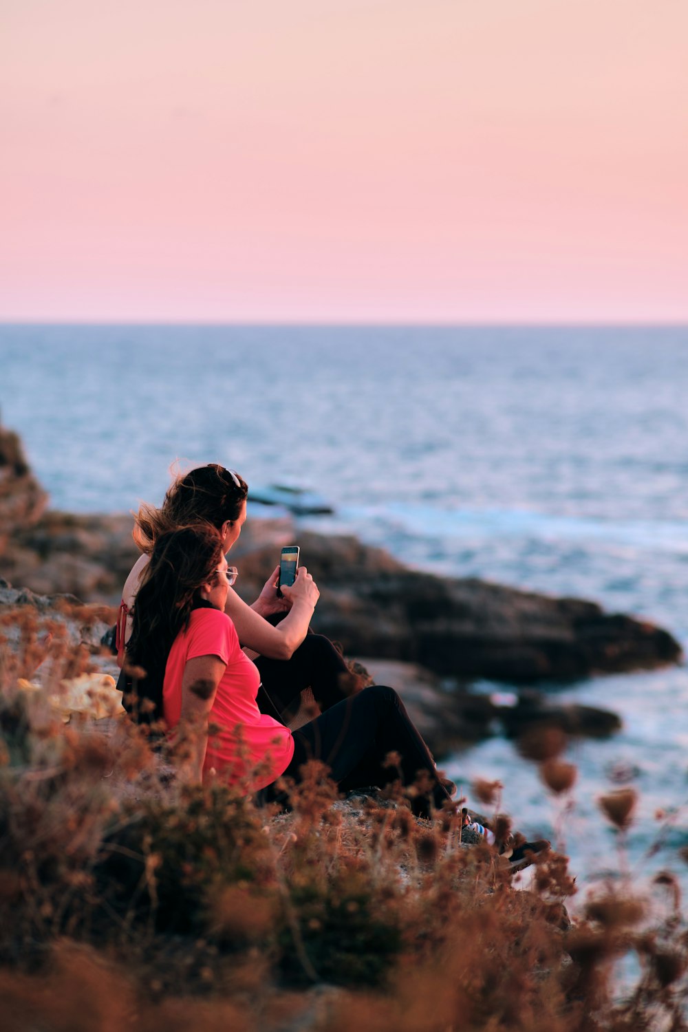 a couple of women sitting on a rock by the water