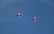 Two red jets fly in formation against a clear blue sky, exhibiting sleek aerodynamic designs.