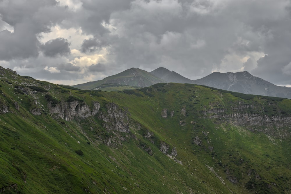 a grassy mountain with clouds above