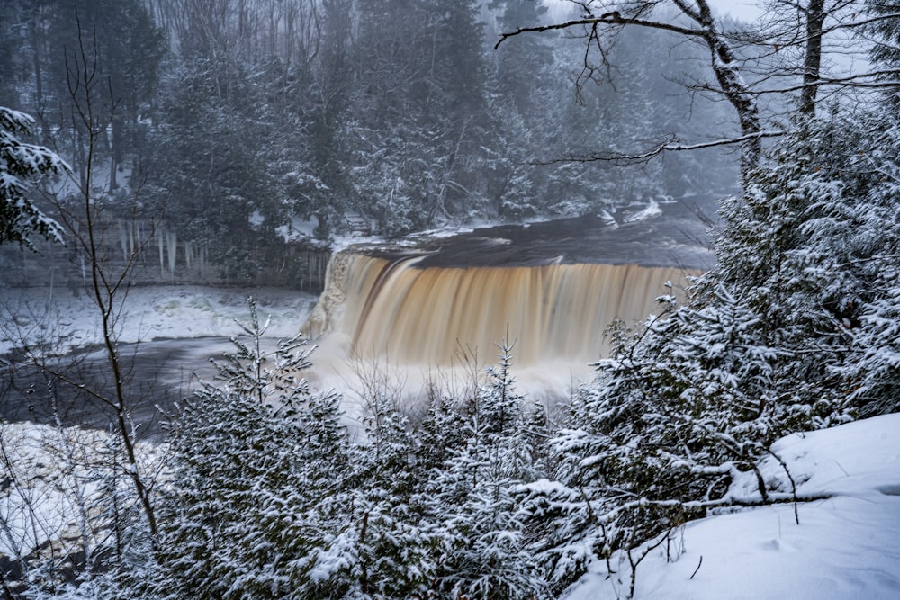 a snowy landscape with trees and a body of water with Tahquamenon Falls in the background