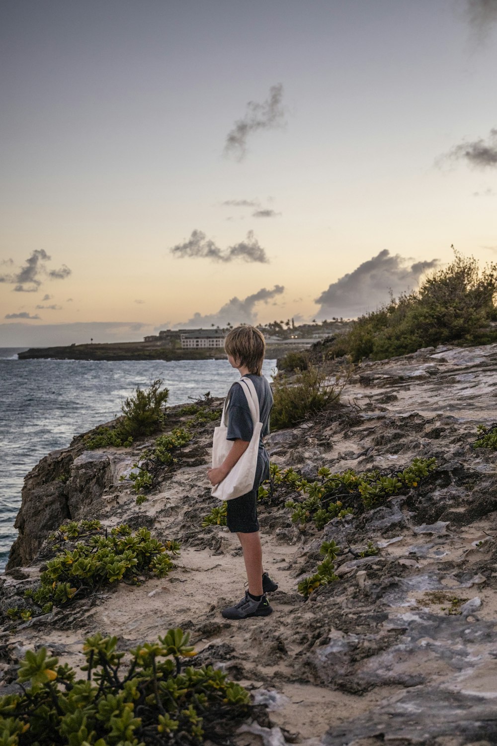 um menino em pé em uma praia rochosa