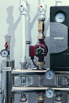 A complex system of pipes and valves with several pressure gauges and a red pump. The setup includes white pipes with red and blue markers, metallic connectors, and a panel with temperature indicators.