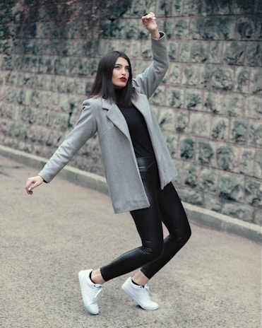 A model wearing layered dark fabrics with subtle metallic accessories, standing against a moody urban wall.