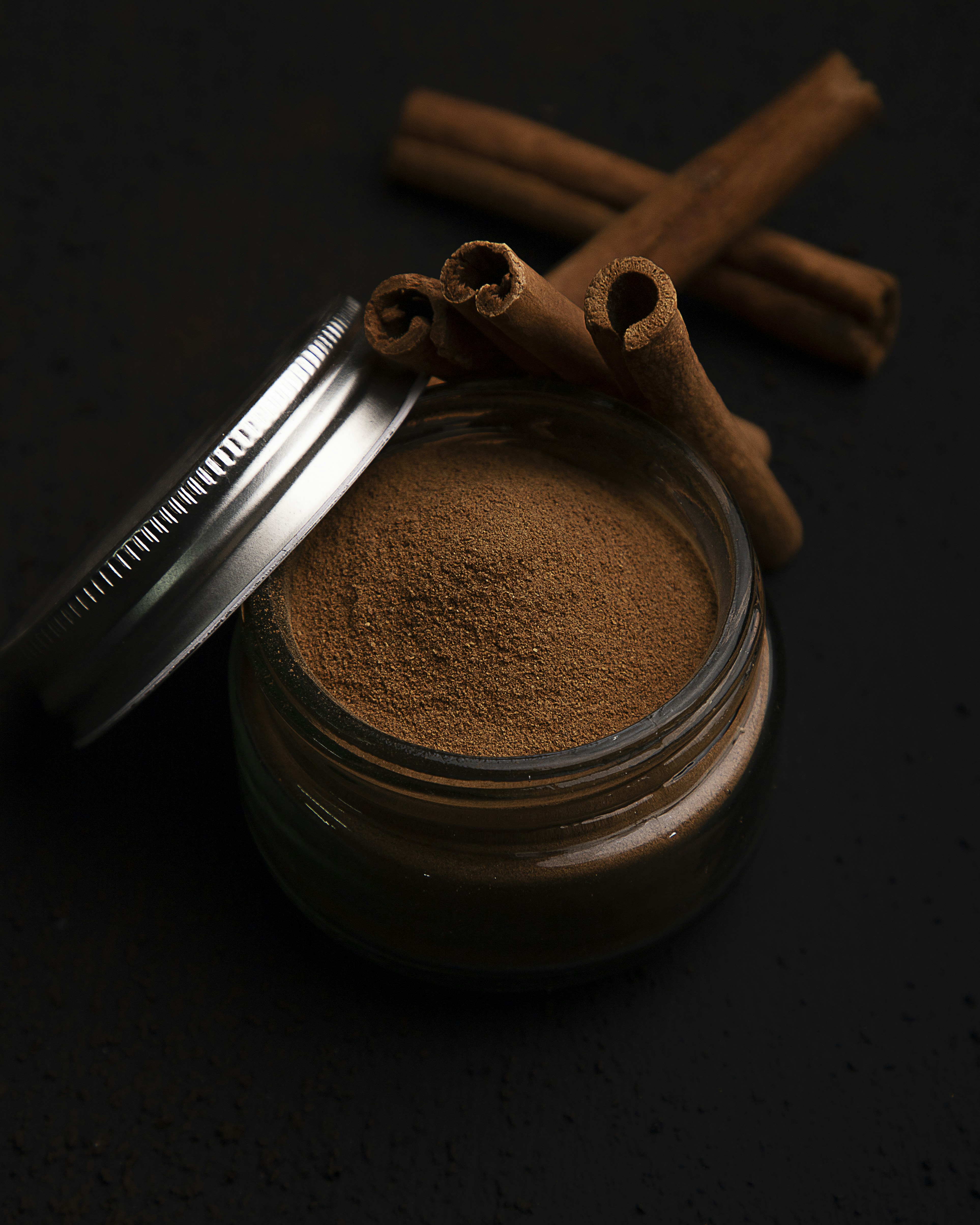 Glass jar of premium hot chocolate powder with marshmallows and cinnamon sticks on rustic background