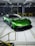 A sleek green sports car with aerodynamic features is parked in an industrial setting. The car has a low profile and glossy exterior, and it is positioned inside a spacious facility with overhead lighting and yellow railings.