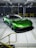A sleek green sports car with aerodynamic features is parked in an industrial setting. The car has a low profile and glossy exterior, and it is positioned inside a spacious facility with overhead lighting and yellow railings.