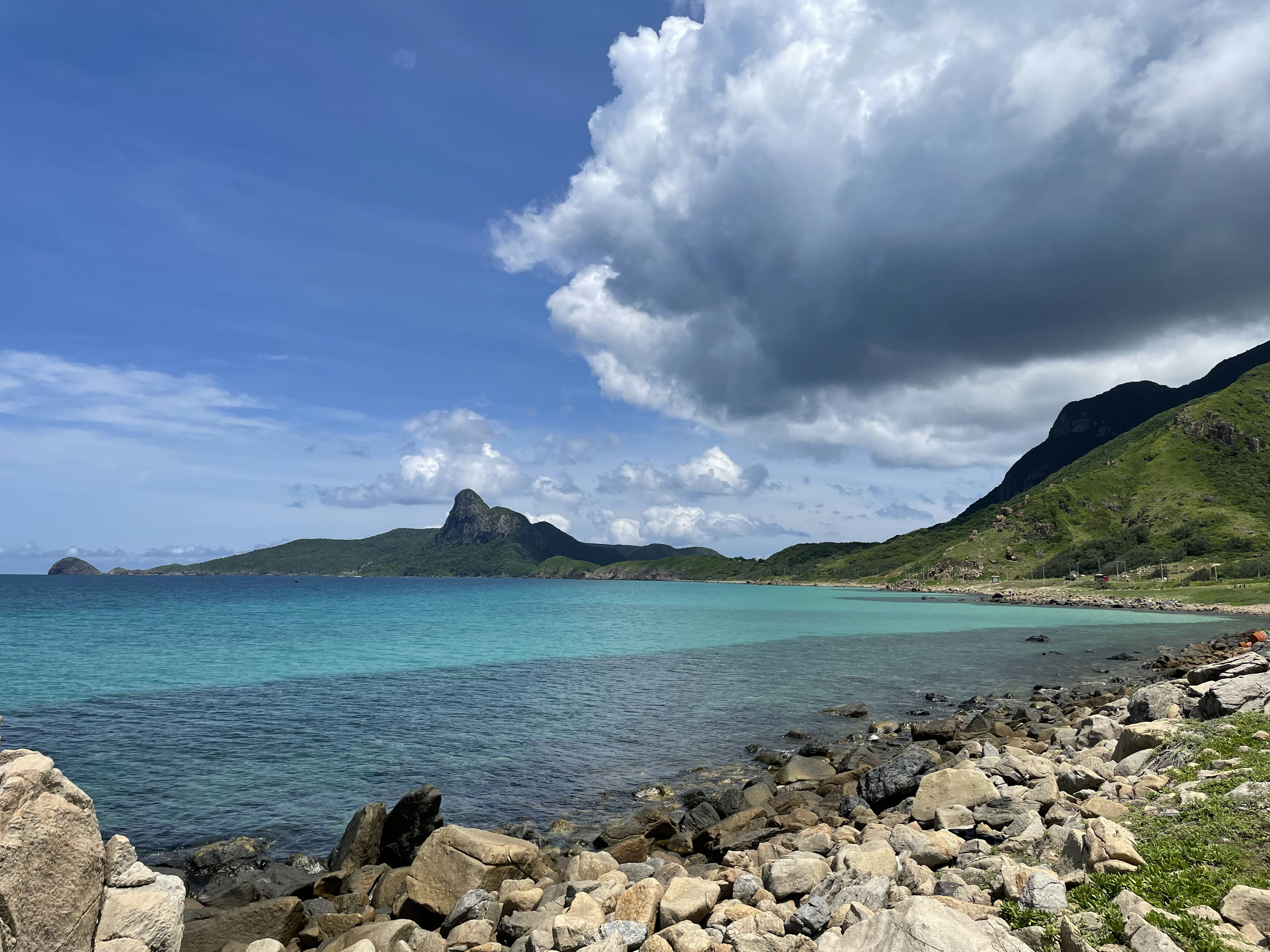 a rocky beach with a body of water and mountains in the background