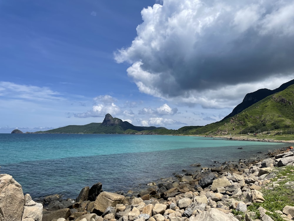 a rocky beach with a body of water and mountains in the background