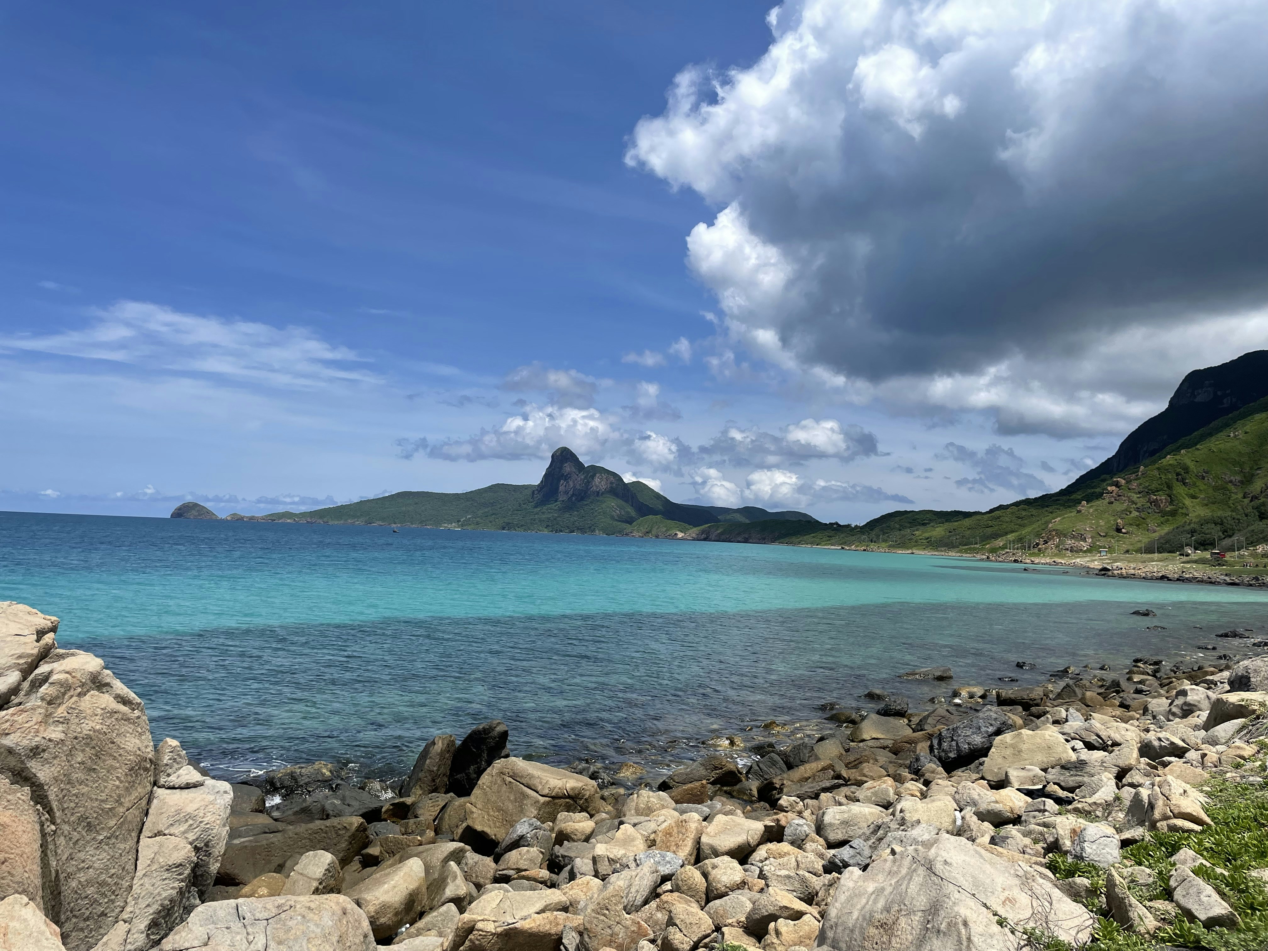 a rocky beach with a body of water and mountains in the background