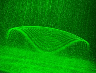 A symmetrical, glowing green pattern resembling a wave or curve with lines and textures that form a seamless, flowing design. The background features a grainy texture that complements the main structure.