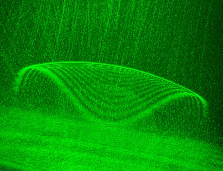 A symmetrical, glowing green pattern resembling a wave or curve with lines and textures that form a seamless, flowing design. The background features a grainy texture that complements the main structure.