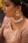 A woman is wearing elaborate jewelry including dangling earrings and a choker necklace adorned with red and silver elements. Her makeup is detailed, with carefully applied eyeliner and lipstick. She wears an embroidered pinkish outfit that shimmers, suggesting a formal or festive occasion. The close-up perspective emphasizes the elegance and intricacy of her attire and accessories.