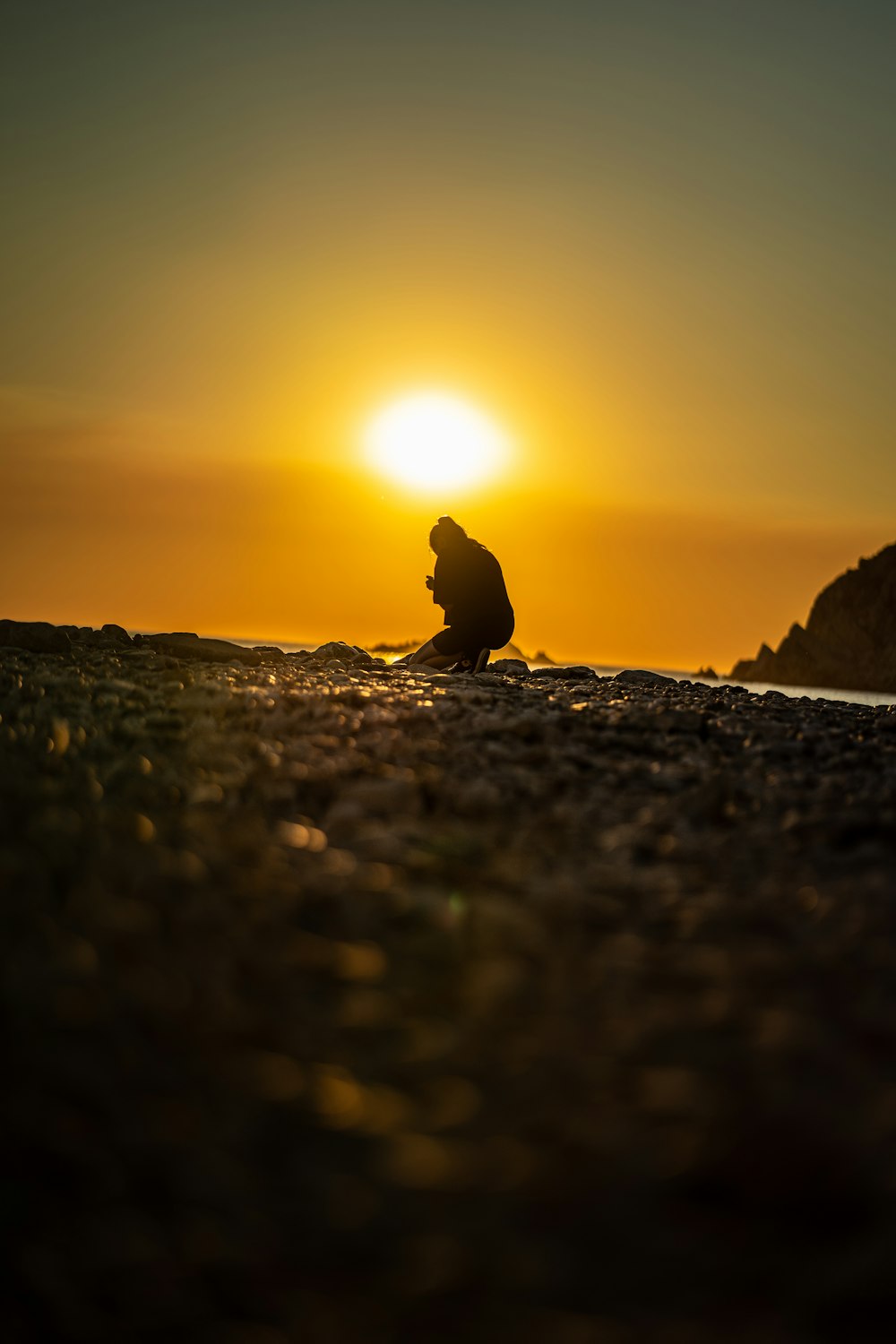 a silhouette of a person on a rocky beach with the sun setting