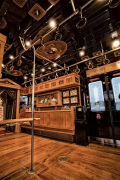 The interior features wooden flooring and cabinetry, elaborate ceiling decorations, and metallic handrails with grips attached. Display cabinets with decorative items are visible, alongside intricately designed glass doors.