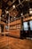 The interior features wooden flooring and cabinetry, elaborate ceiling decorations, and metallic handrails with grips attached. Display cabinets with decorative items are visible, alongside intricately designed glass doors.