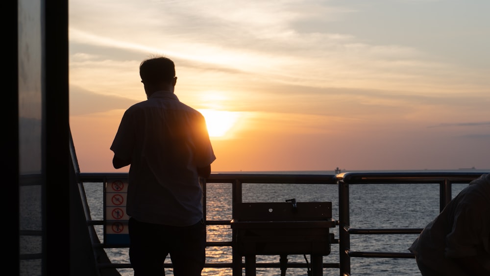 a person standing on a balcony looking out at the sunset