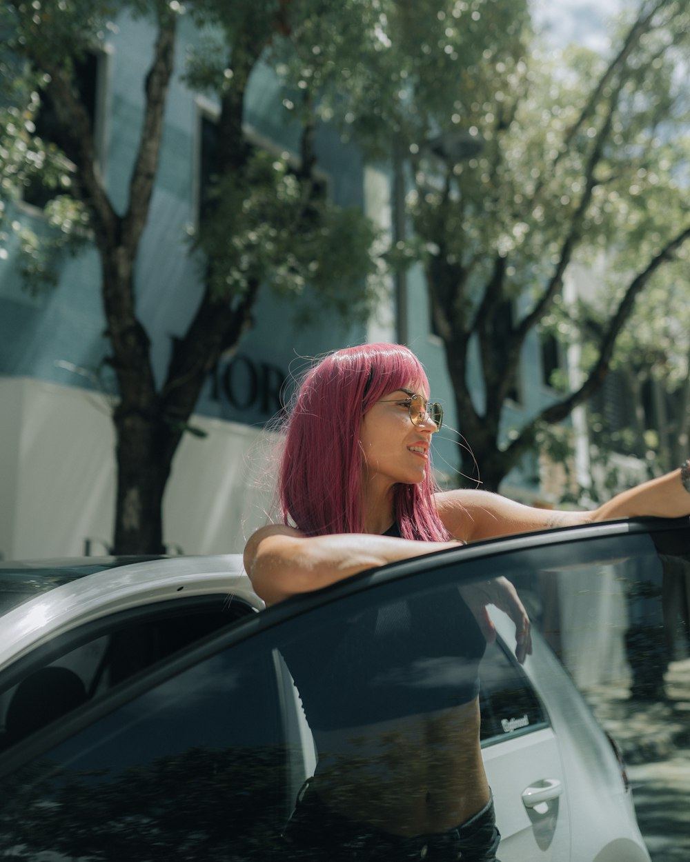 a woman in a pink wig leaning on a car