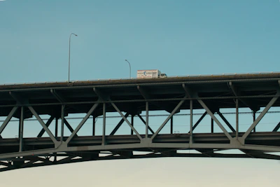 A pink steel logistics truck crossing a bridge over a river, symbolizing connection and movement.