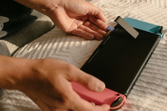 A person is inserting a microSD card into a gaming console on a textured white surface. The console has blue and red controllers attached.