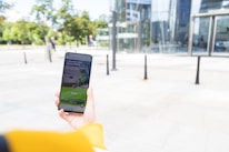 A person holding a smartphone with a financial application open on the screen, standing outside a modern glass building. The background shows a plaza with trees and pedestrians.