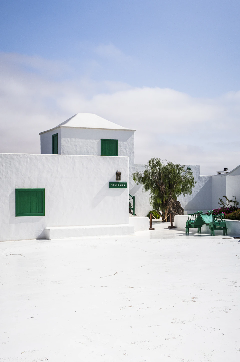 White building with green shutters and roof on street corner features two windows and door