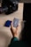 A person holds a compact Samsung external hard drive near a laptop. Nearby, there are small memory cards and a camera with a large lens.