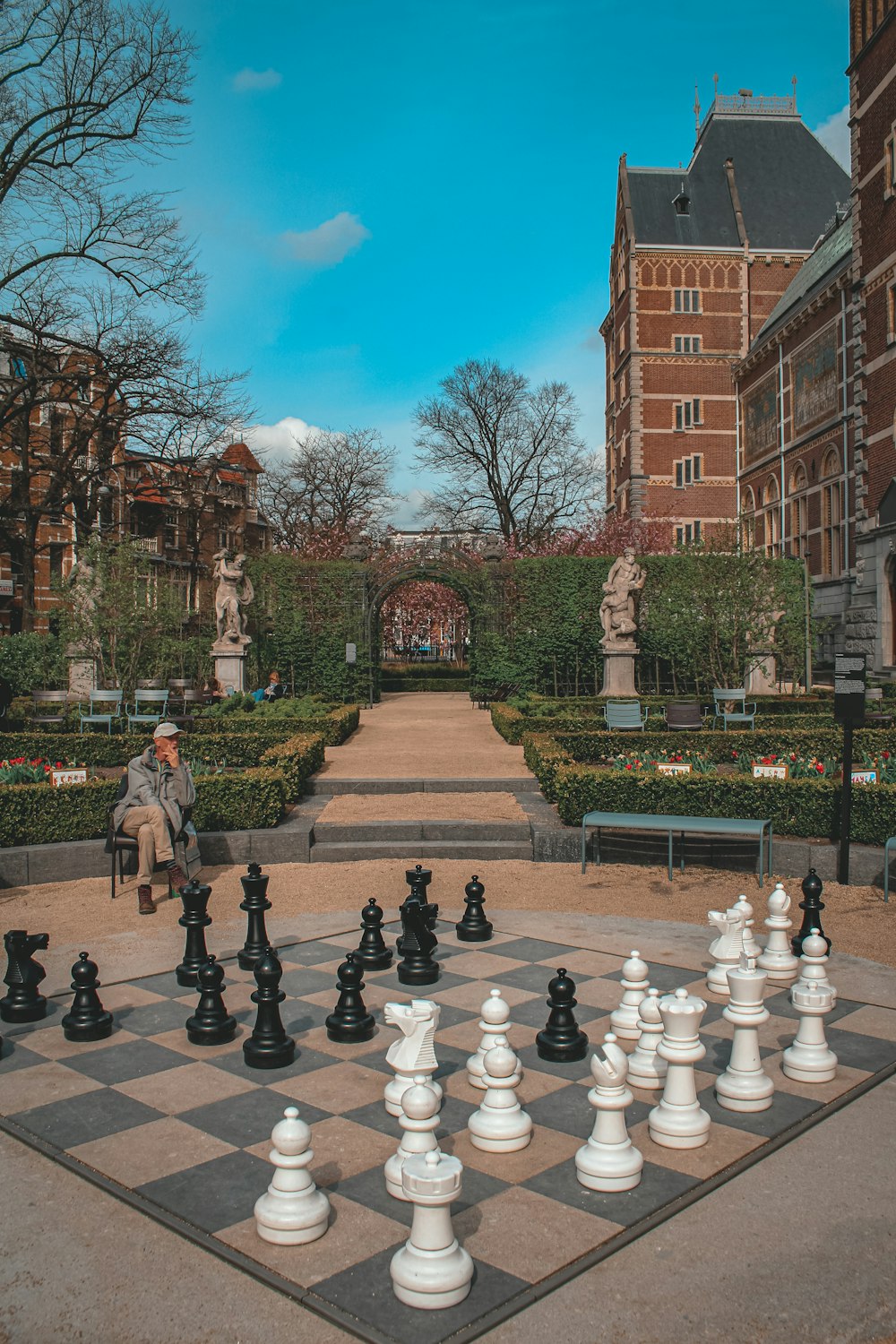 a person sitting on a bench in a courtyard with a chess board