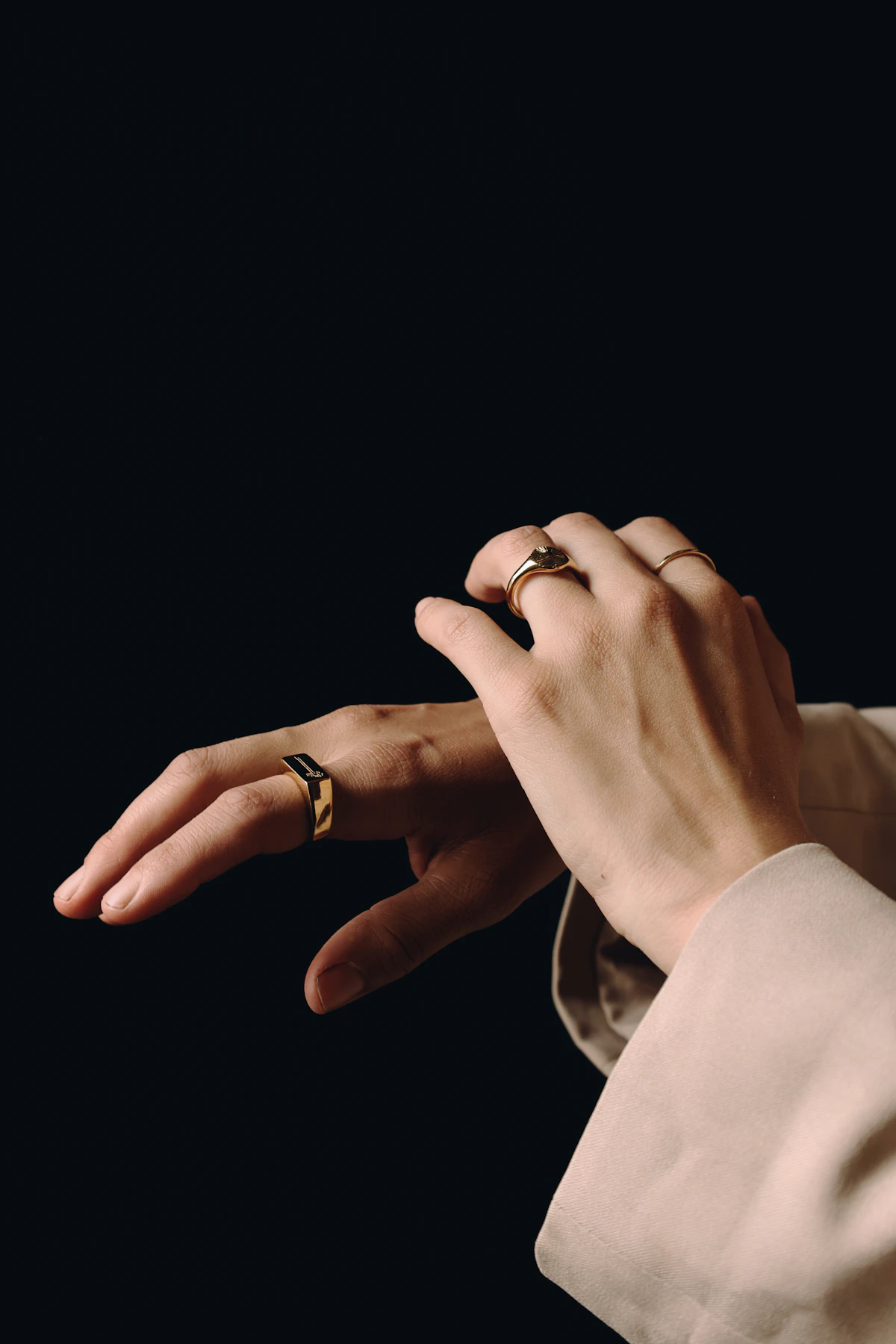 Hands wearing stacked gold rings against a dark background