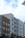 A series of modern multi-story apartment buildings with various exteriors including wood, brick, and siding. The buildings have numerous windows and small balconies. The sky above is partly cloudy with patches of blue visible. A few tree branches can be seen on the left.