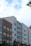 A series of modern multi-story apartment buildings with various exteriors including wood, brick, and siding. The buildings have numerous windows and small balconies. The sky above is partly cloudy with patches of blue visible. A few tree branches can be seen on the left.