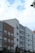 A series of modern multi-story apartment buildings with various exteriors including wood, brick, and siding. The buildings have numerous windows and small balconies. The sky above is partly cloudy with patches of blue visible. A few tree branches can be seen on the left.