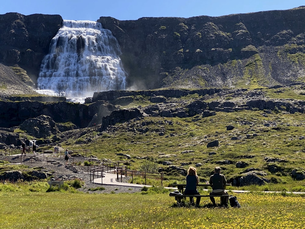 a couple sitting on a bench in front of a waterfall
