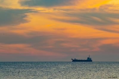 A calm sea at sunset with a large cargo ship sailing smoothly on the horizon.