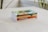 A stack of four books is neatly arranged on a light-colored surface with blurred greenery in the background. Each book is authored by Derek Prince, featuring titles like Protection from Deception and The Coming Revival.