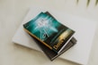 A book titled 'The Gifts of the Spirit' by Derek Prince is placed on top of a closed laptop and another notebook with an elastic band. The book cover features a serene, spiritual design with teal and golden hues, depicting a foggy landscape scene with a path leading toward a distant light.
