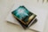 A book titled 'The Gifts of the Spirit' by Derek Prince is placed on top of a closed laptop and another notebook with an elastic band. The book cover features a serene, spiritual design with teal and golden hues, depicting a foggy landscape scene with a path leading toward a distant light.