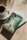 A cup of coffee sits on a saucer next to two books placed on a sunlit surface. The top book has a cover depicting a person walking between parted waters, with the title 'Prayers and Proclamations' by Derek Prince. The lighting casts soft shadows on the surface.