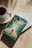 A cup of coffee sits on a saucer next to two books placed on a sunlit surface. The top book has a cover depicting a person walking between parted waters, with the title 'Prayers and Proclamations' by Derek Prince. The lighting casts soft shadows on the surface.
