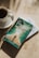 A cup of coffee sits on a saucer next to two books placed on a sunlit surface. The top book has a cover depicting a person walking between parted waters, with the title 'Prayers and Proclamations' by Derek Prince. The lighting casts soft shadows on the surface.
