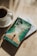 A cup of coffee sits on a saucer next to two books placed on a sunlit surface. The top book has a cover depicting a person walking between parted waters, with the title 'Prayers and Proclamations' by Derek Prince. The lighting casts soft shadows on the surface.