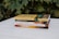 A stack of five books rests on a white wooden surface. Each book cover features text and distinct designs, with titles like 'Prophetic Guide to the End Times' and 'War in Heaven' by Derek Prince. The background consists of lush green leaves, offering a natural backdrop to the scene.